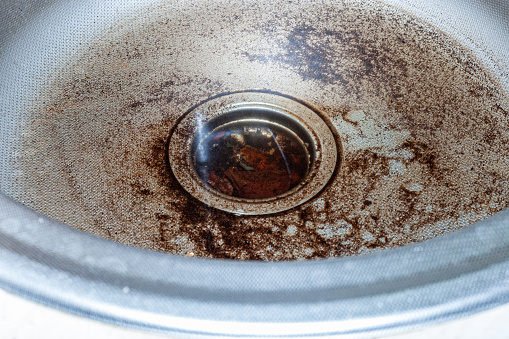The drain of the stainless steel sink for washing dishes is clogged with water and food particles.