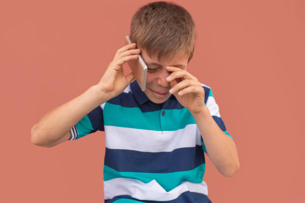 плачущий маленький мальчик разговаривает по телефону от боли - bullying child teasing little boys стоковые фото и изображения