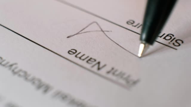 Close-up of a person signing a business contract with a black ballpoint pen.