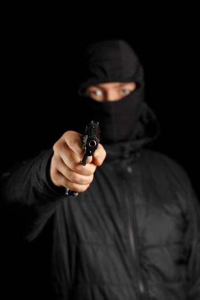 Man with a gun on a black background. The gun is in focus, the masked man is blurred.