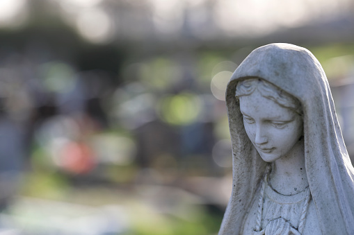 Head of sombre-looking stone angel in a churchyard. Selective focus. Surrey, England.