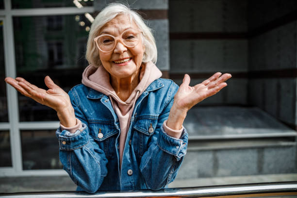 Happy mature woman standing outdoors stock photo Smiling old lady in jeans jacket is enjoying time in open air grandmother stock pictures, royalty-free photos & images