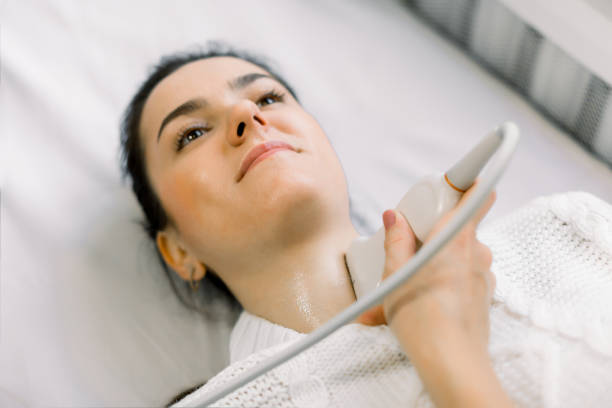 close up top angle portrait of a young woman smiling while having her neck and thyroid examined by her doctor using ultrasound scanner - ultrasound cancer healthcare and medicine thyroid gland imagens e fotografias de stock