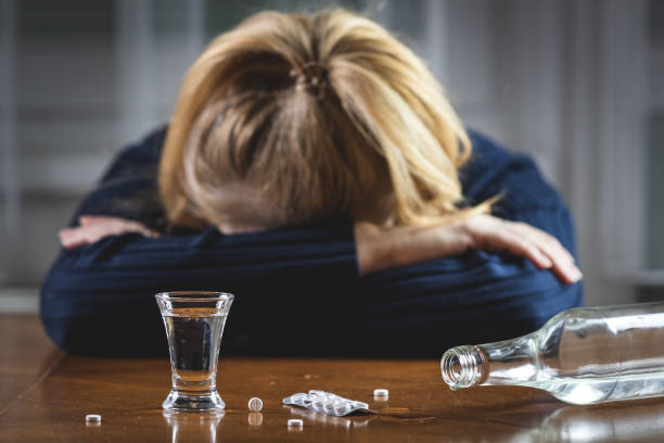 Woman sleeping after drug overdose and drinking vodka Pills, shot glass and bottle with hardliquor on table. Drugs and alcohol abuse is social issues alcoholism alcohol addiction drunk stock pictures, royalty-free photos & images