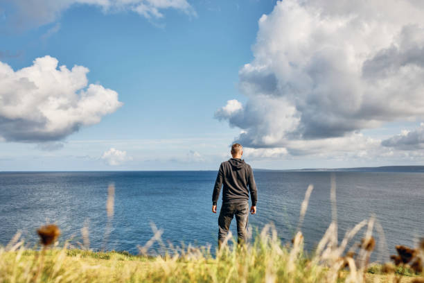 istock Man stood alone looking out over an idyllic bright sunny seascape at Pentire, Newquay, Cornwall on a Septembers day. 1203364124