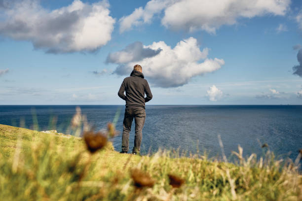 istock Man stood alone looking out over an idyllic bright sunny seascape at Pentire, Newquay, Cornwall on a Septembers day. 1203364146