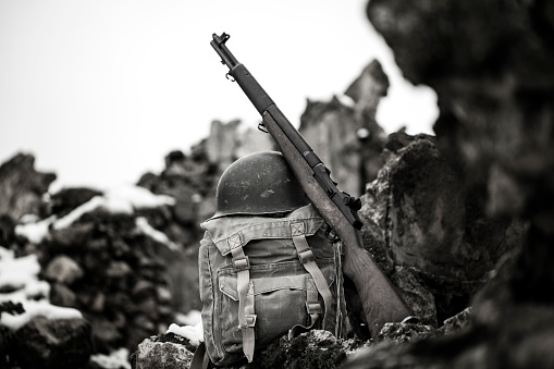 US Army M1 rifle and helmet on soldier backpack in battlefield