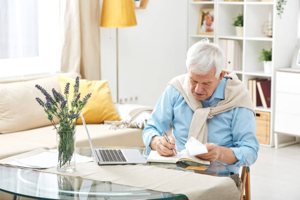 istock Senior casual man with white hair making notes in notebook while working at home 1203365561