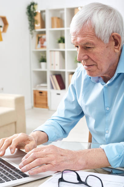 istock Aged retired man pressing keys of laptop keypad while surfing in the net 1203365652