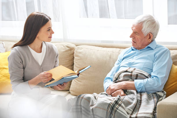 istock Young female social worker with open book discussing it with senior man 1203365675