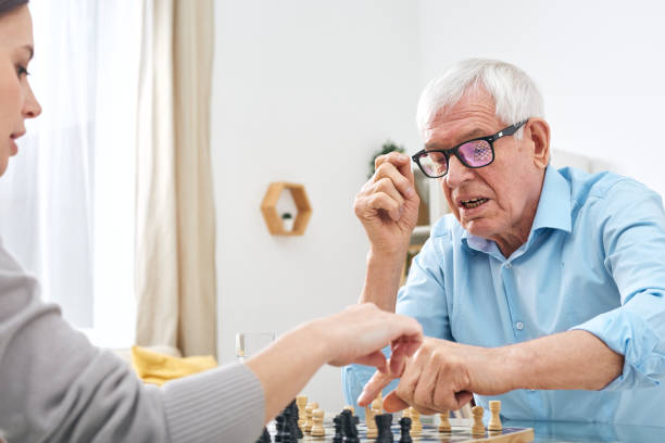 istock Senior disable man in eyeglasses and shirt playing chess with social worker 1203365681