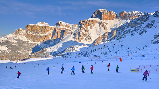 Dolomites, Italy - January 20, 2020: Skiers on the slopes, early morning, with Sella group in the background, lit at sunrise, in Dolomiti Superski domain, Italy, on the Sellaronda circuit.