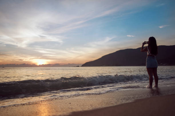 istock Woman at the beach taking pictures 1203371849