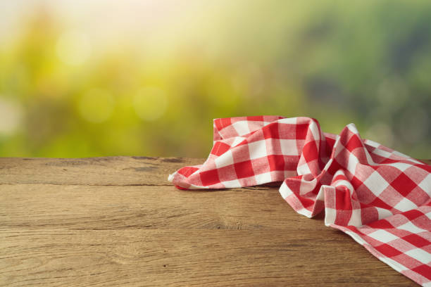 istock Empty wooden table with red checked tablecloth over green bokeh background. Spring and easter mock up for design. 1203375864