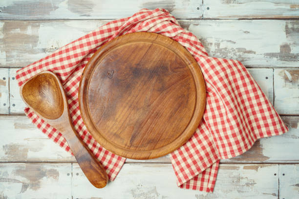 istock Round pizza board with red checked tablecloth on rustic wooden table Kitchen, cooking or baking mock up background for design. 1203375898