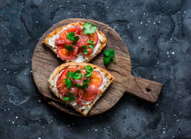 istock Smoked salmon, tomatoes, cream cheese, cilantro sandwich on a rustic cutting board on a dark background, top view 1203378173