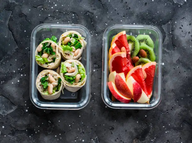 Healthy diet food lunch box - fruit and chicken, beans, green salad pita bread on a dark background, top view. Sweet b savory lunch box
