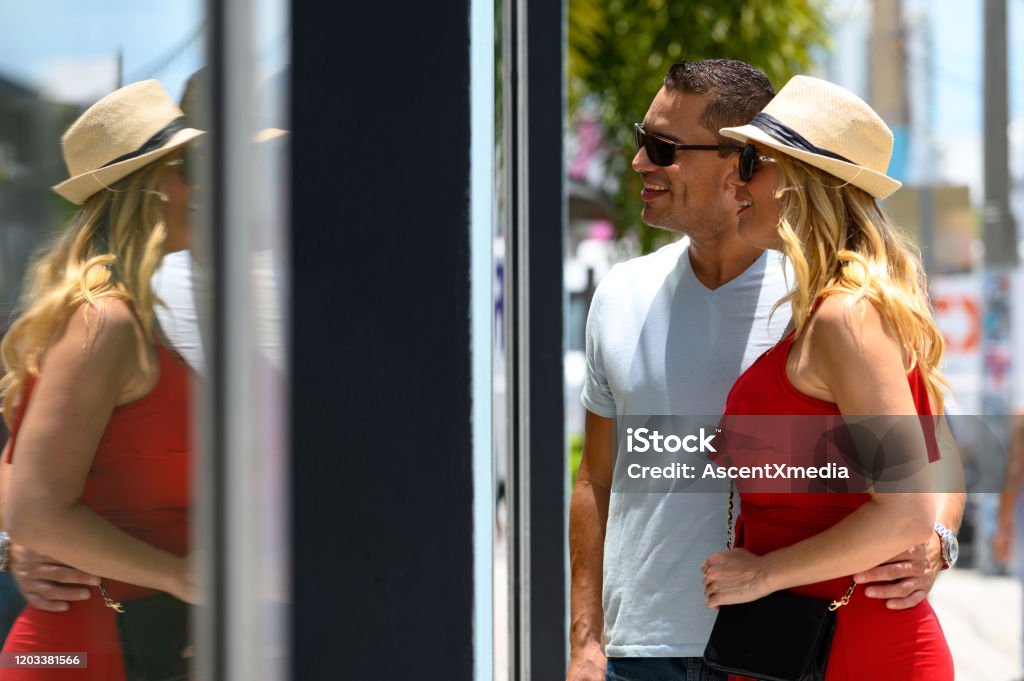 Smiling couple looking at store window in city Smiling man with arm around woman looking at store window. Happy couple is shopping in city. They are in casuals. Miami Stock Photo