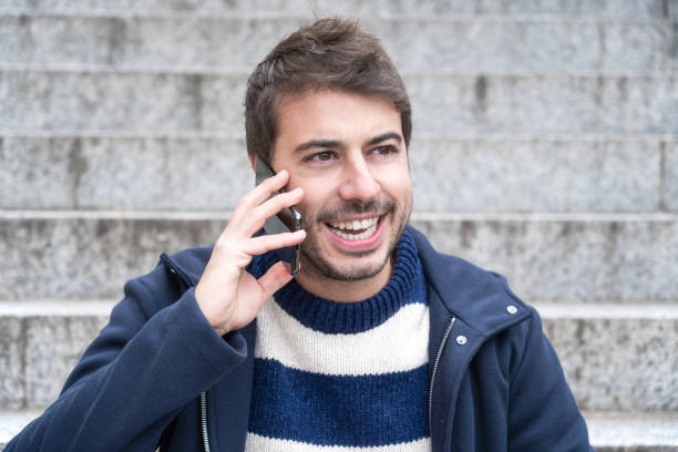istock Young handsome man, smiling, talking on the phone sitting on the stairs. 1203382447