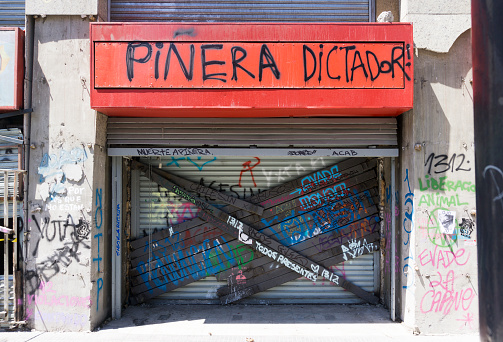 Santiago, Chile - November 2, 2019: Damaged shop access in Santiago de Chile after the demostration, with grafitti and welded steel bars on the shutters to prevent looting