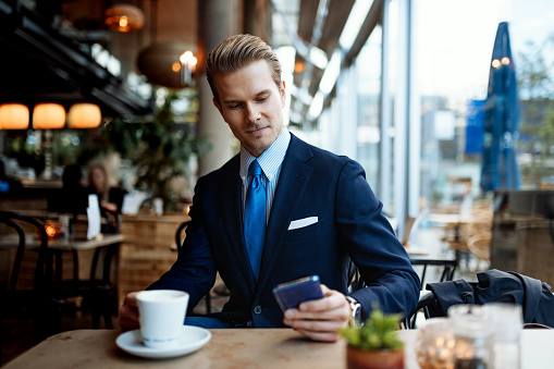 Portrait of young successful business person in modern suit with necktie, working on laptop and using mobile phone during coffee break