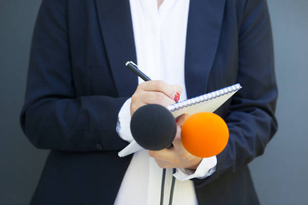 istock Woman journalist or reporter at press conference, writing notes, holding microphone. Journalism concept. 1203396709