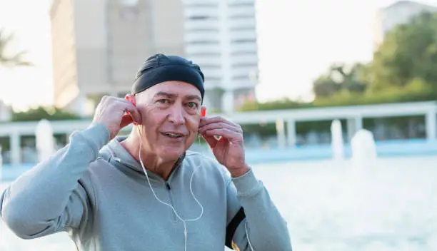 A mature man in his 50s in the city, smiling as he puts on earphones to listen to music.