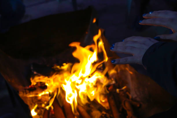 A woman warms her hands near an open fire from a bonfire in metal box at night. Theme of Poverty and Overcoming Challenges.