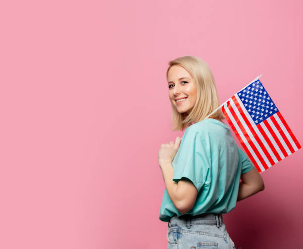 Beautiful blonde woman with USA flag on pink background stock photo