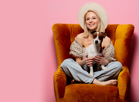 Beautiful blonde womanwith a dog in an armchair on pink background