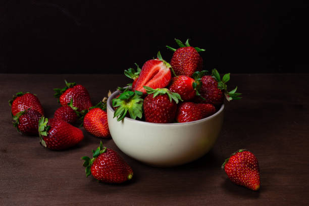 istock Fresh strawberries in ceramic bowl on dark wooden background. Selective focus. - Image 1203427232