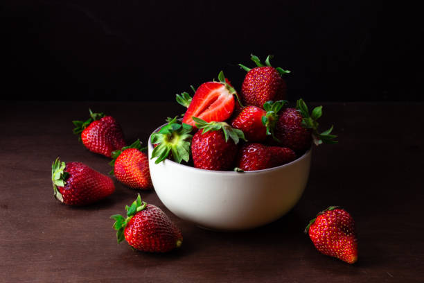 istock Fresh strawberries in ceramic bowl on dark wooden background. Selective focus. - Image 1203427283