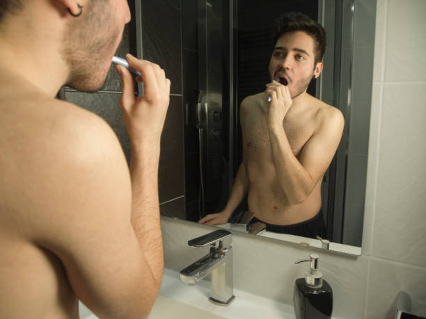 ハンサムな白人ティーンエイジャーの肖像画は、彼の歯を磨き、鏡から反射 - shaved head ストックフォトと画像