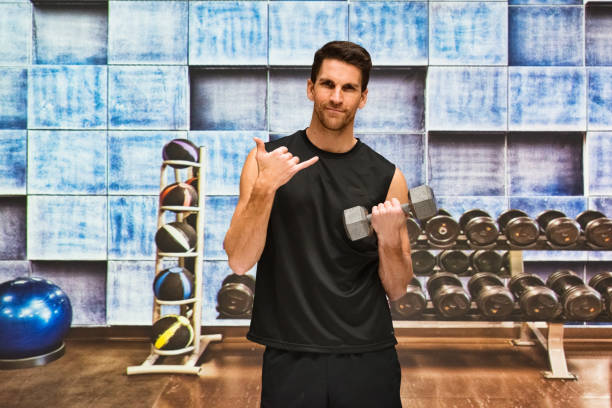 Male athlete doing relaxation exercise at the health club in the gym wearing sports clothing and being active with dumbbell and using fitness ball One person of male athlete doing relaxation exercise at the health club in the gym wearing sports clothing who is serious who is show shaka sign ( hang loose ) and being active with dumbbell and using fitness ball 11313 stock pictures, royalty-free photos & images