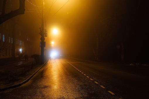 Foggy misty night road illuminated by street lights.