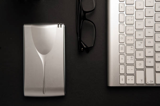 istock Conceptual table for informatic work, silver-colored desktop hard drive with lenses, partial view of computer keyboard, black background 1203435219