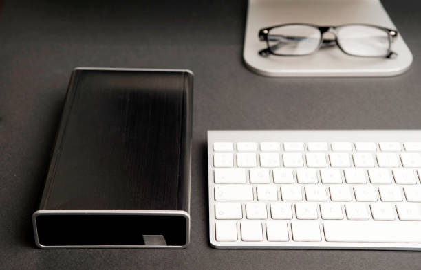 istock Black external hard drive and parcial base computer view, keyboard, black glasses, black background 1203435220