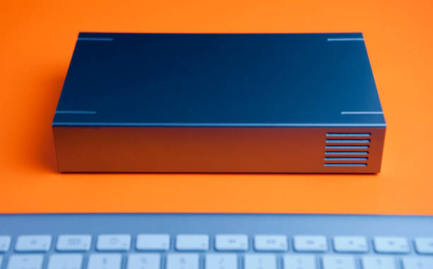istock front view, blue hard drive with vent, partial view of keyboard on orange background 1203435268