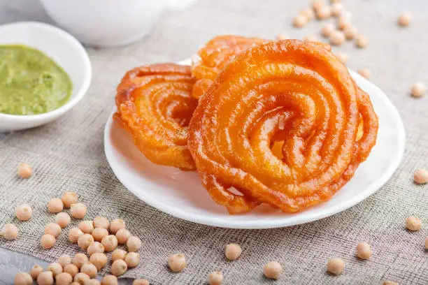 traditional indian candy jalebi in white plate with mint chutney on a gray concrete background. side view, close up.