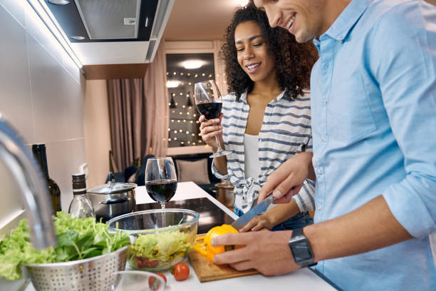 istock Romantic Date. Young multiethnic couple standing at kitchen cooking dinner wife drinking wine while husband cutting vegetables close-up laughing cheerful 1203441619