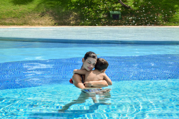 madre (37 años) e hijo (4 años) en la piscina dando un abrazo amoroso. - enfold fotografías e imágenes de stock