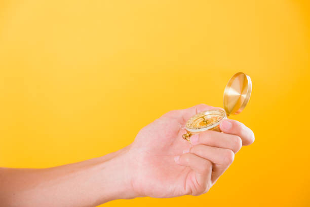 Hand holding antique brass compass isolated on yellow background with copy space for text