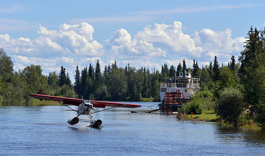 Float plane landing on the Chena River in Fairbanks, Central Alaska, old time steamboat in the background.