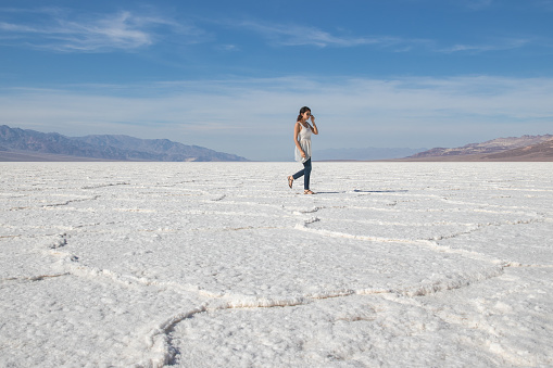 Beautiful young mixed race woman walking in jeans, white shirt and sunglasses on a hot sunny summer day. Death Valley National Park, California.