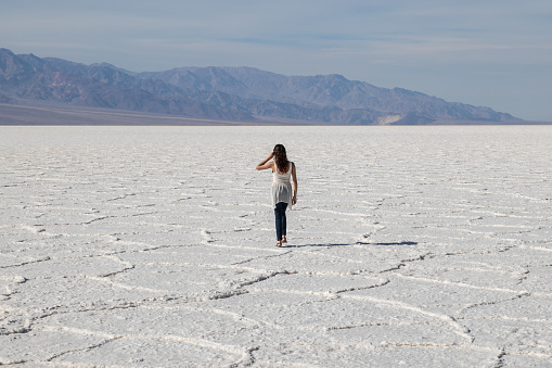 Mixed race woman walking away through bright white salt flats of Death Valley National Park, California. Hot summer bright day.