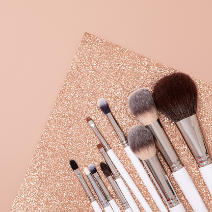 Make-up brush in flat lay style on soft glitter beige and gold background. Top view