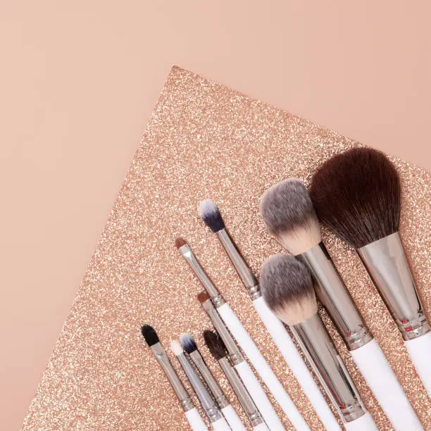 Photo of Make-up brush in flat lay style on soft glitter beige and gold background. Top view