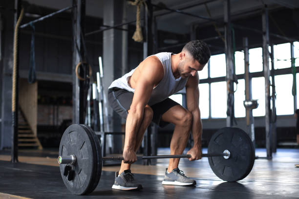 istock Muscular man working out in gym doing exercises with barbell at biceps. 1203487955