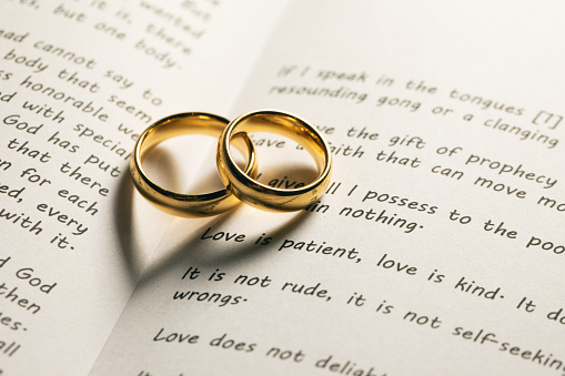 Two golden wedding rings on Holy bible book with heart shaped shadow close up
