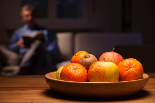 istock Fruit bowl on a table with a man reading on a sofa in the background 1203505532